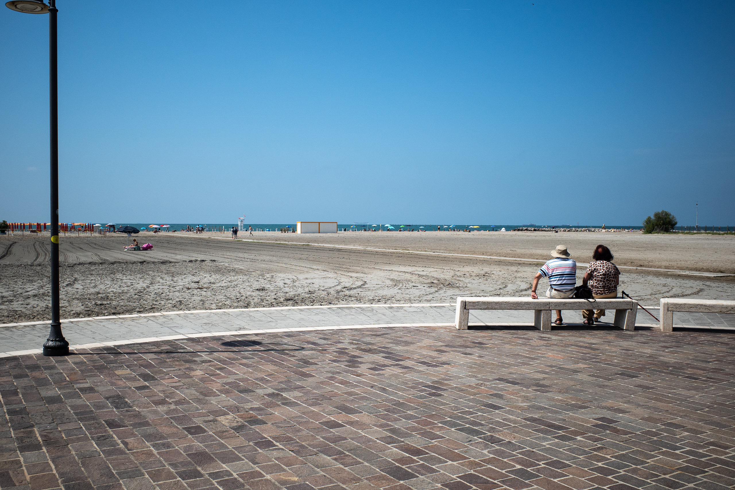 Auf der Bank an der Promenade, vor sich den weiten Strand